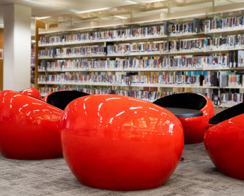 Library shelves with rows of books and bright red pod chairs in the foreground, symbolising changes underway as part of the Library’s transition.